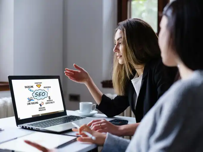 Search Engine Optimization (SEO) Concept On Computer Screen With Two Businesswomen In The Office